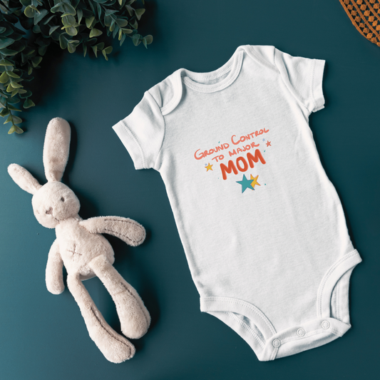White baby onesie with 'Ground Control to Major Mom' text and a plush toy on a dark green background